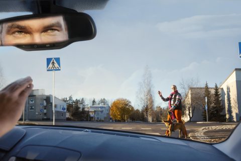 Autoilija antaa tilaa suojatiellä kävelijälle. Molemmat tervehtivät toisiaan.