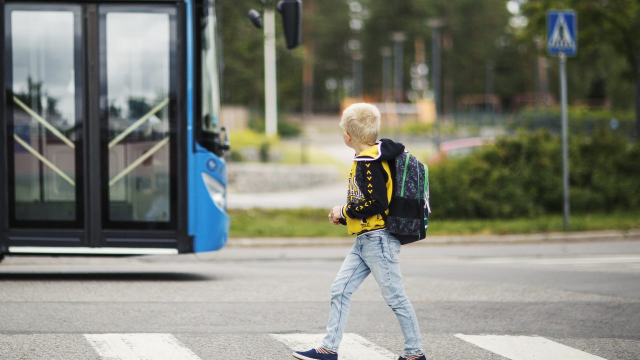 lapsi ylittää suojatietä. taustalla on linja-auto.