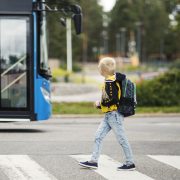 lapsi ylittää suojatietä. taustalla on linja-auto.