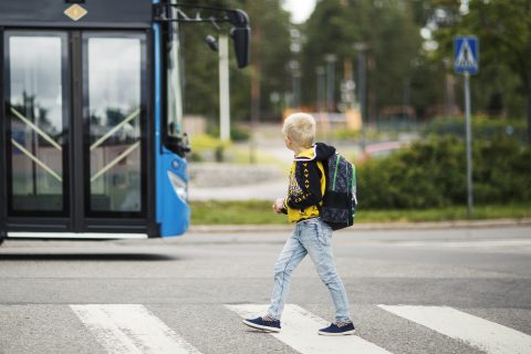 lapsi ylittää suojatietä. taustalla on linja-auto.