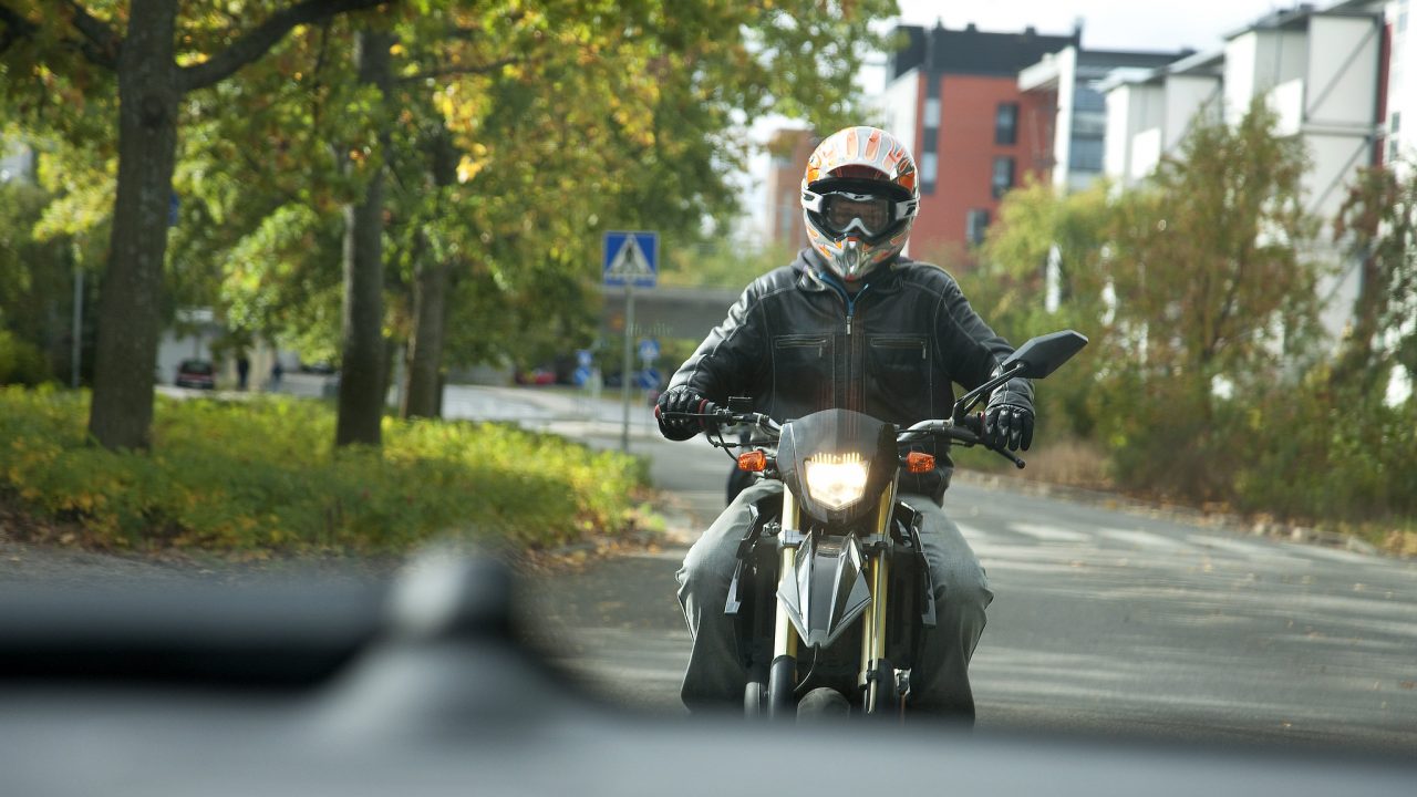 Mopoilija liikenteessä kypärä päässä. Mopoilijalla on yllään hyvät turvavarusteet.