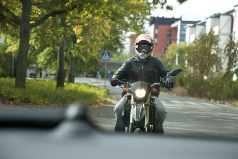 Mopoilija liikenteessä kypärä päässä. Mopoilijalla on yllään hyvät turvavarusteet.