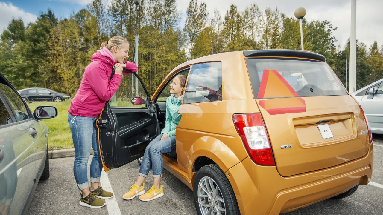 Kaksi nuorta mopoauton vierellä.