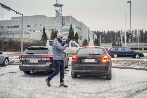 Jalankulkija moikkaa parkkipaikalla autoilijaa