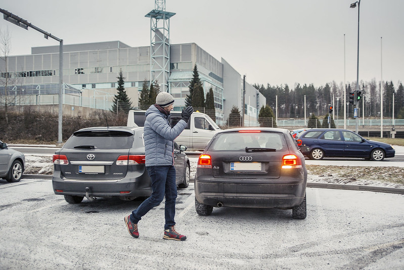 Jalankulkija moikkaa parkkipaikalla autoilijaa