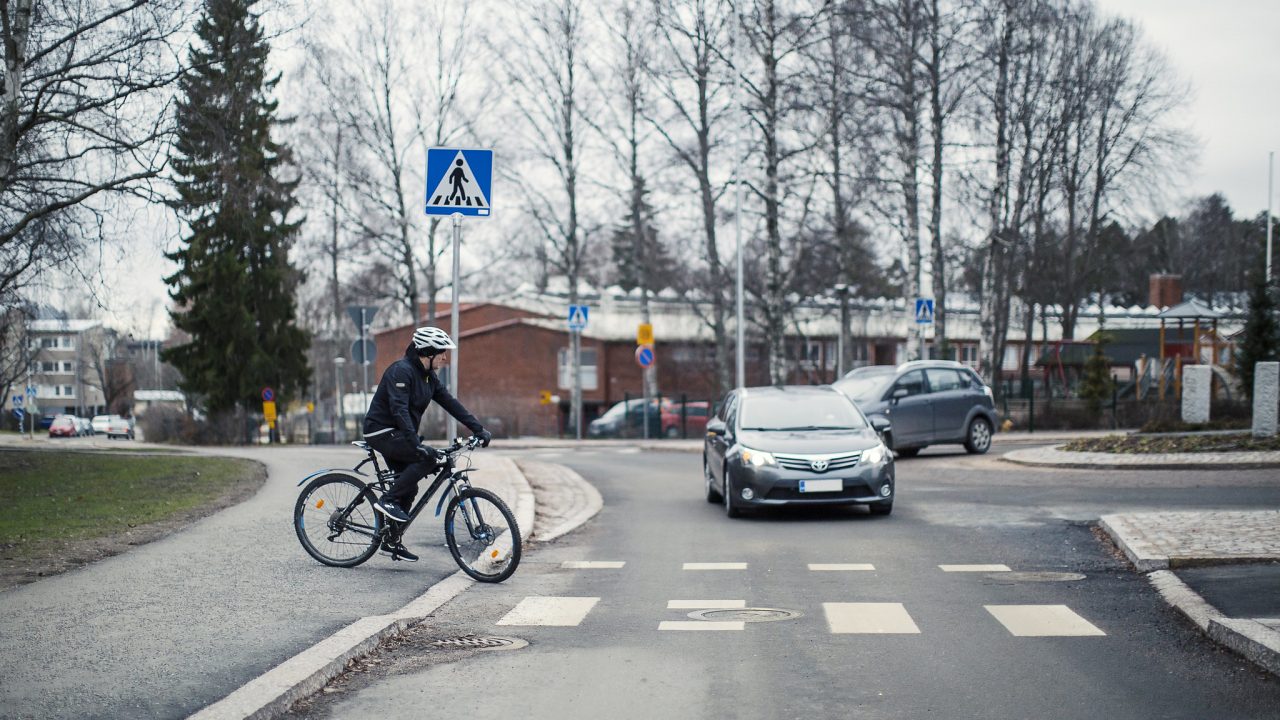 Pyöräilijä ylittää tien, liikenneympyrästä poistuva auto väistää.