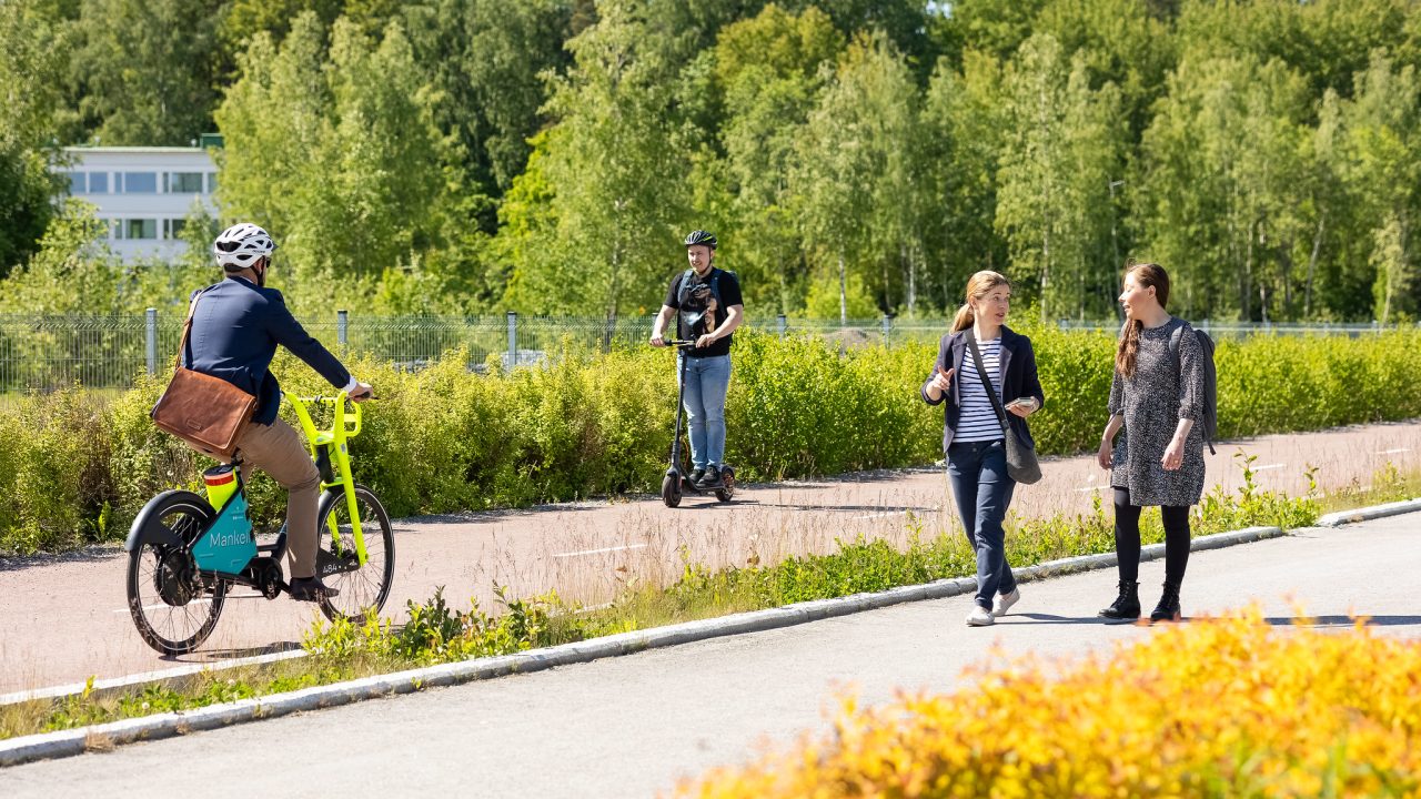 Pyöräilijä, kävelijät ja sähköpotkulauta liikenteesä.