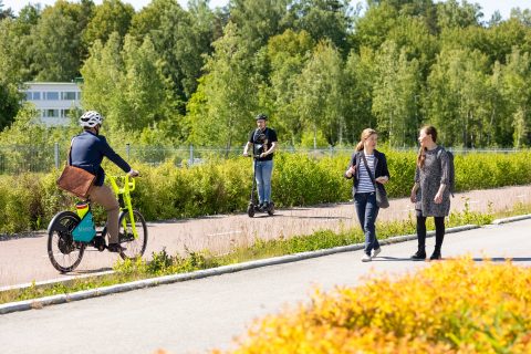 Pyöräilijä, kävelijät ja sähköpotkulauta liikenteesä.