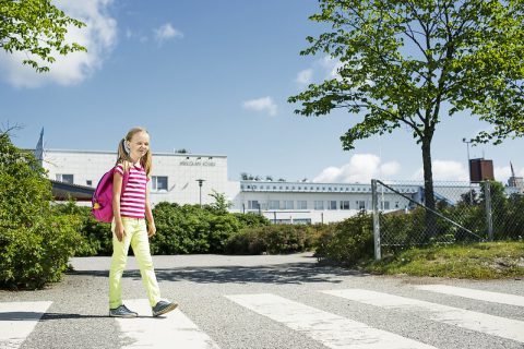 Lapsi ylittää suojatietä koulun edustalla.