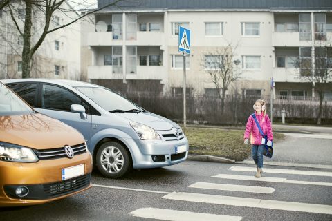 Lapsi ylittämässä suojatietä. Kaksi autoa pysähtynyt suojatien eteen antamaan tilaa lapselle.