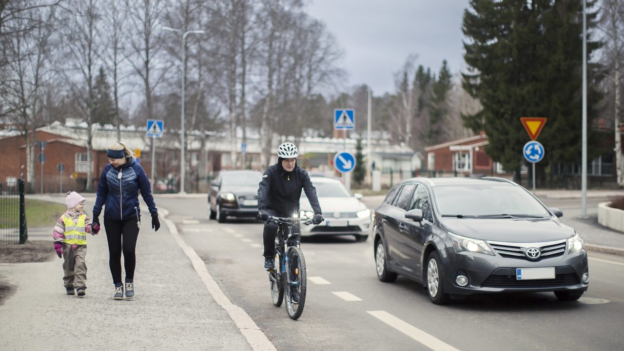 Jalankulkijat jalkakäytävällä, pyöräilijä pyöräkaistalla, auto ajoradalla.