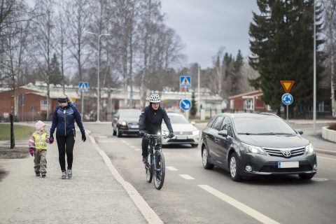 Jalankulkijat jalkakäytävällä, pyöräilijä pyöräkaistalla, auto ajoradalla.