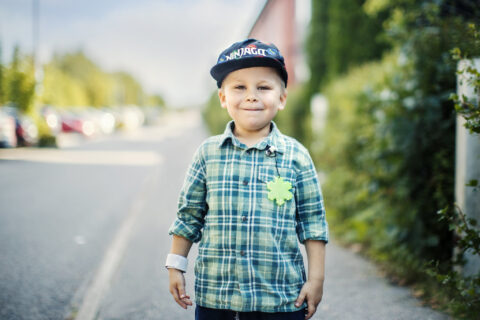 Lapsi seisoo jalkakäytävällä. Paidassa on kiinni heijastin.