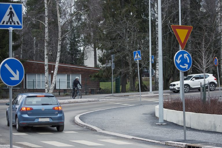 Auto poistuu liikenneympyrästä ja pyöräilijä ylittää tietä