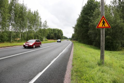 Autoja maantiellä ja jalankulkijoista varoittava liikennemerkki tien laidassa.