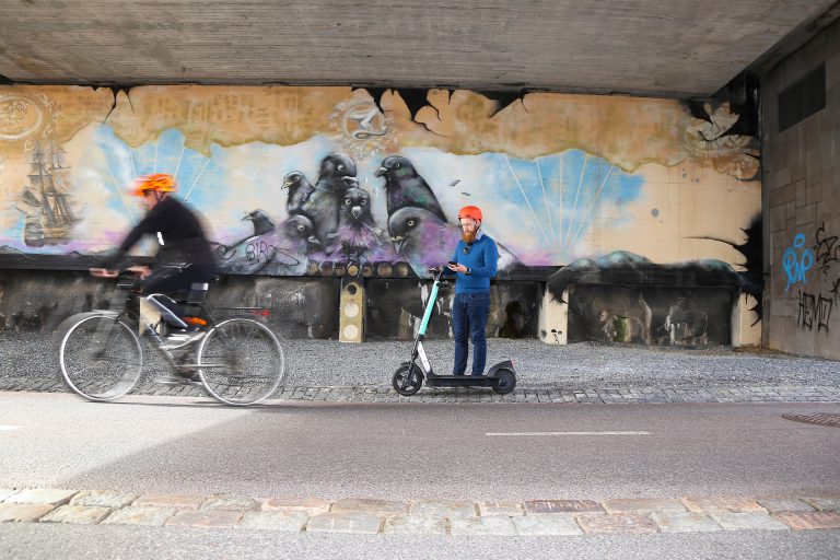 Sähköpotkulautailija on pysähtynyt tien sivuun katsomaan puhelintaan.