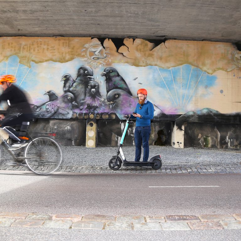 Sähköpotkulautailija on pysähtynyt tien sivuun katsomaan puhelintaan.
