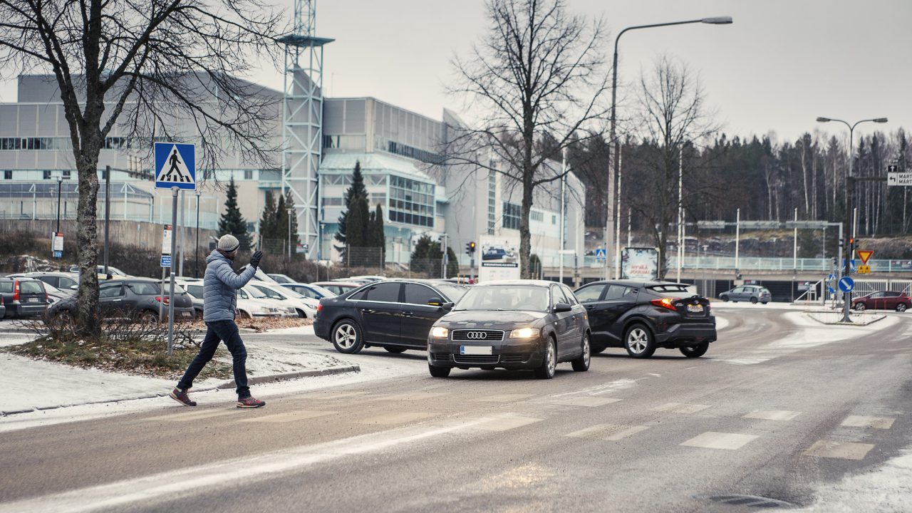 Jalankulkija ylittää suojatien ja heilauttaa autoilijalle kättään kiitokseksi.