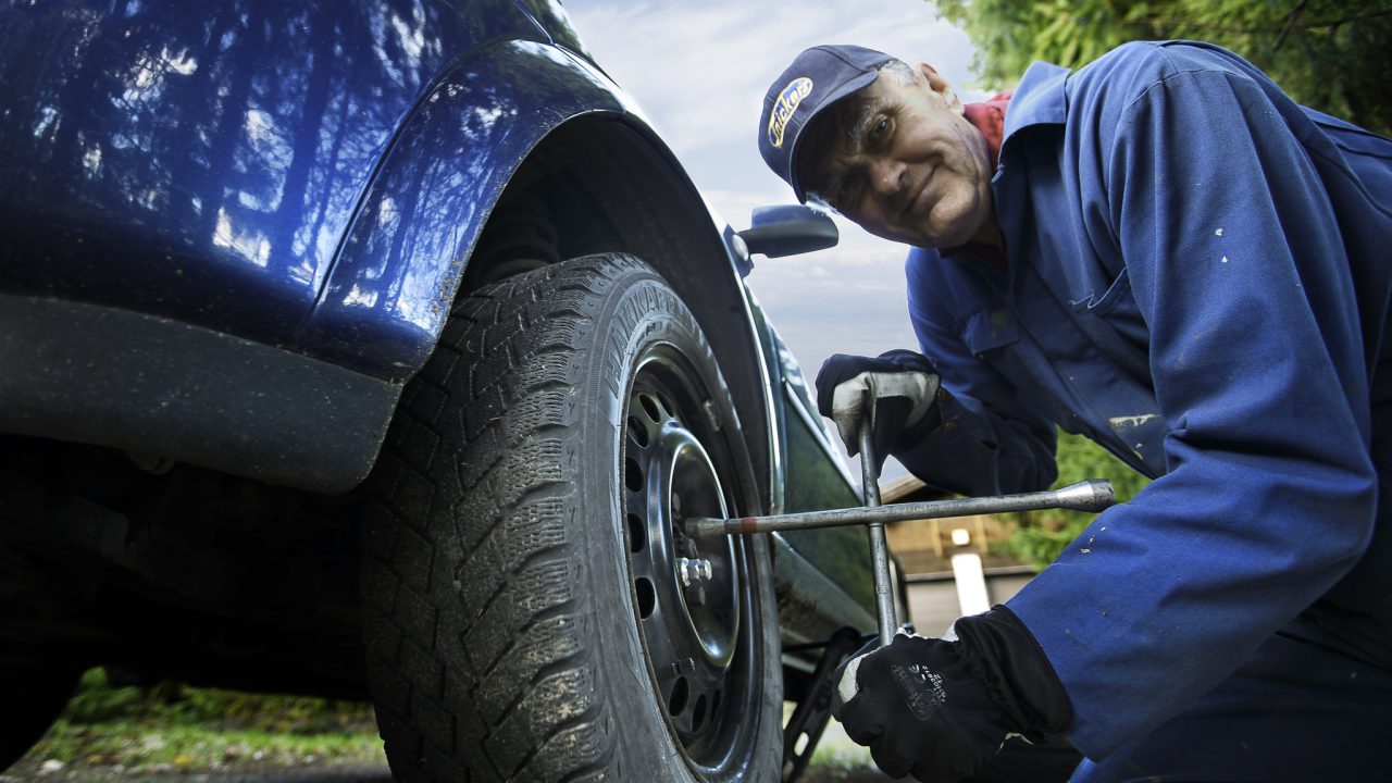 Mies vaihtaa renkaita autoon.