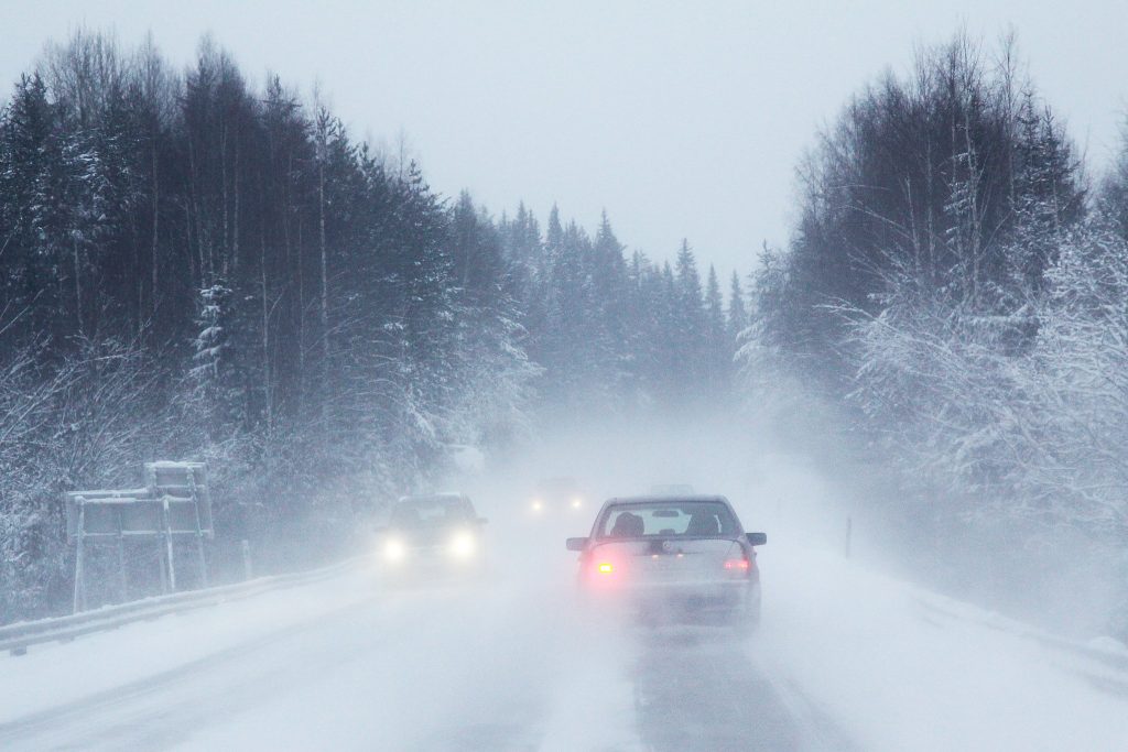 Autoja ajaa maantiellä, lumi pöllyää.