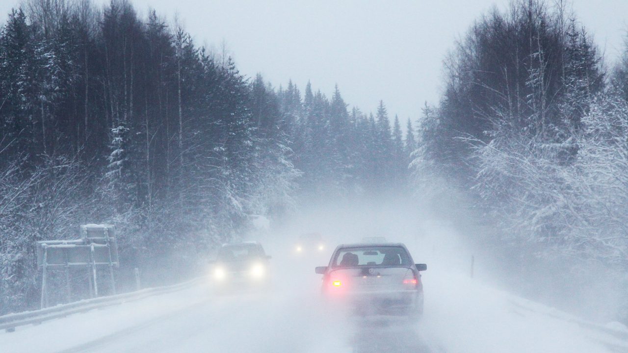 Autoja ajaa maantiellä, lumi pöllyää.