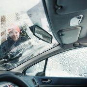 Henkilö putsaamassa auto lumesta ja jäästä ennen liikkeellelähtöä.