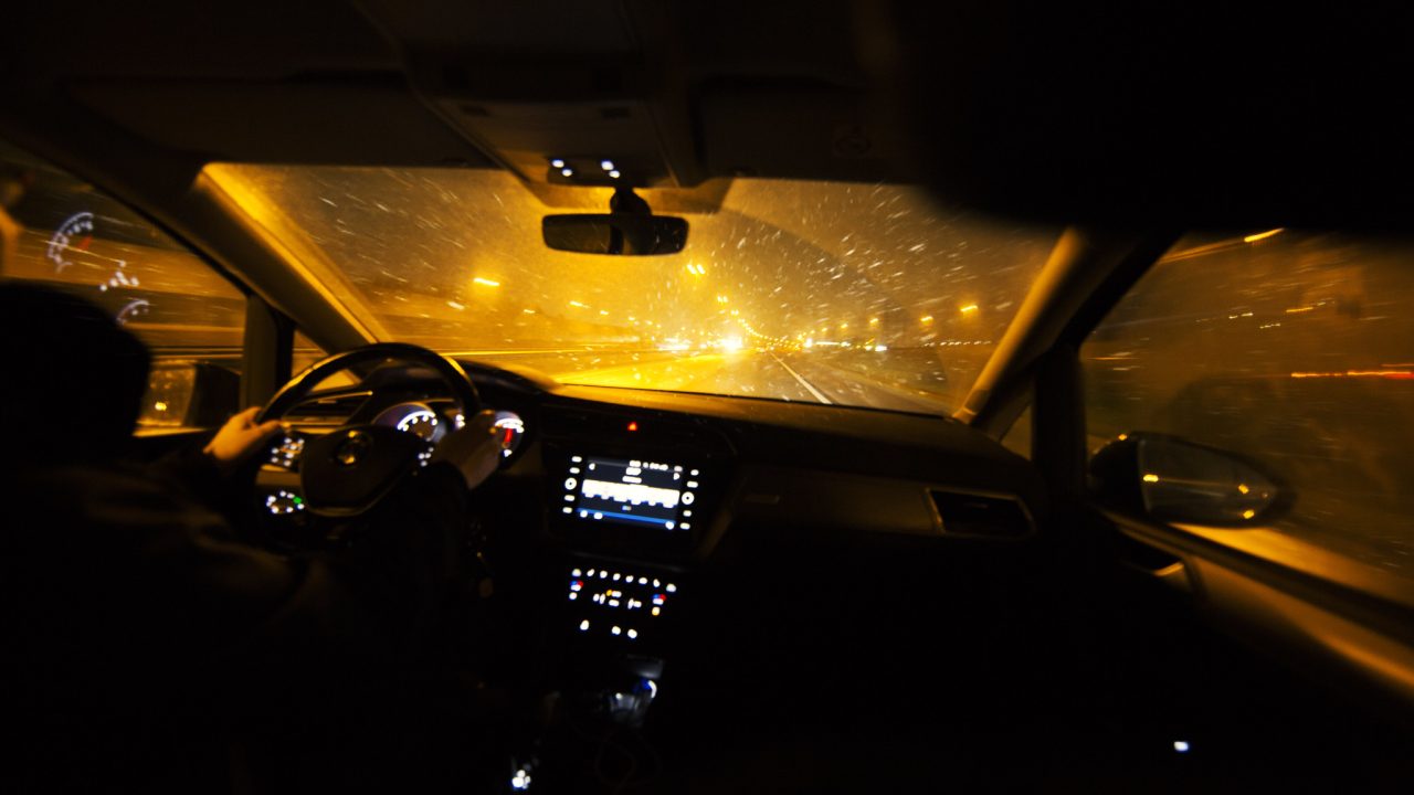 Sateinen ja pimeä näkymä auton tuulilasin läpi.