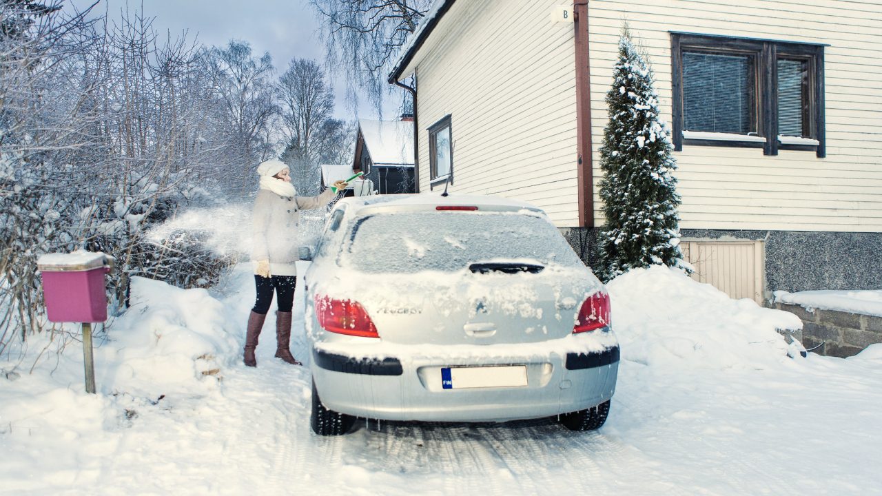 Henkilö harjaa lunta auton katolta.