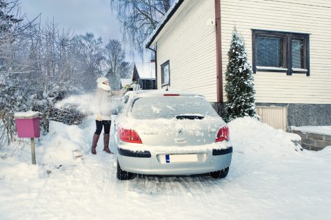 Henkilö harjaa lunta auton katolta.