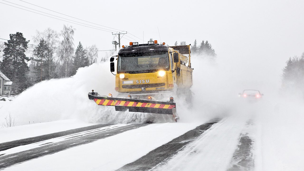 Aura-auto työntää lunta pöllyävässä lumessa.