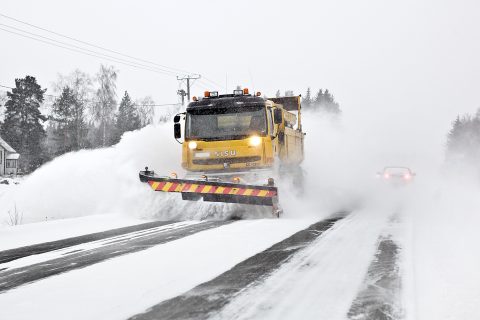 Aura-auto työntää lunta pöllyävässä lumessa.