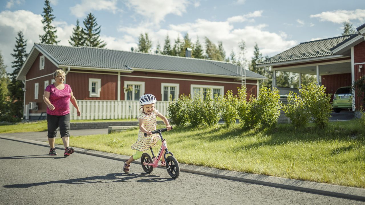 Lapsi potkupyöräilee isovanhemman kanssa.