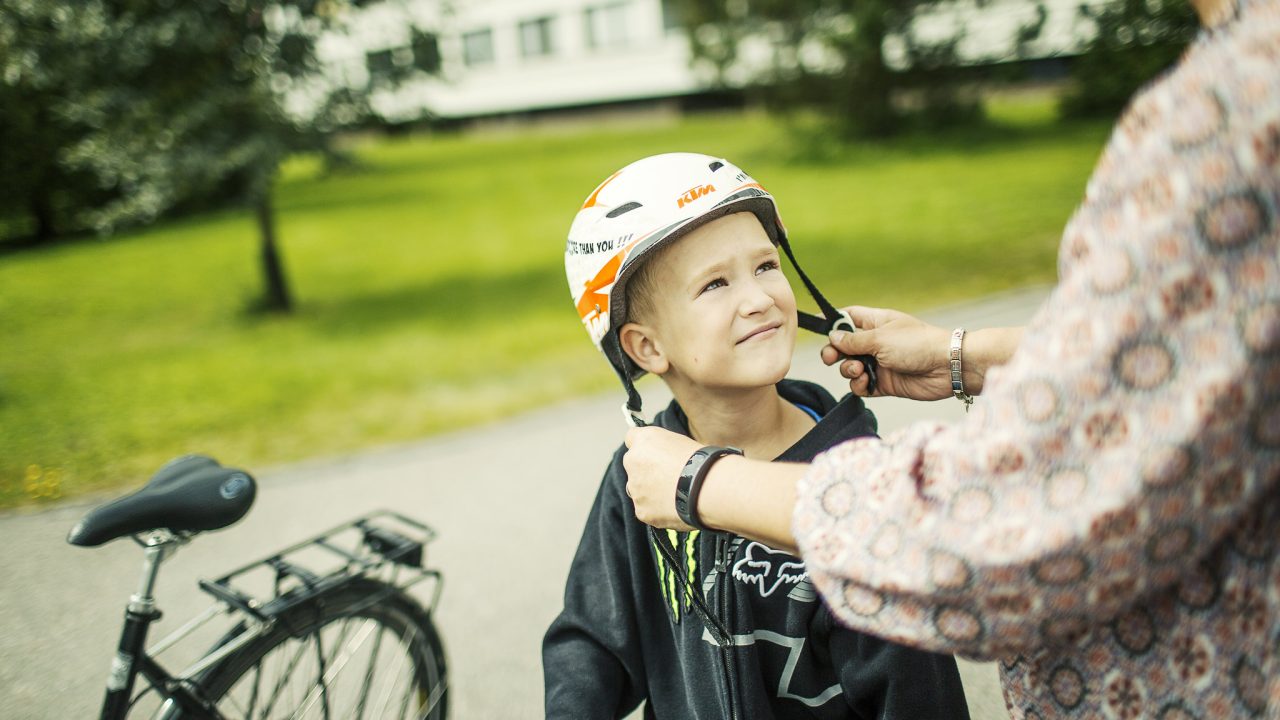 Lapsi laittaa kypärän päähän ja aikuinen opastaa.