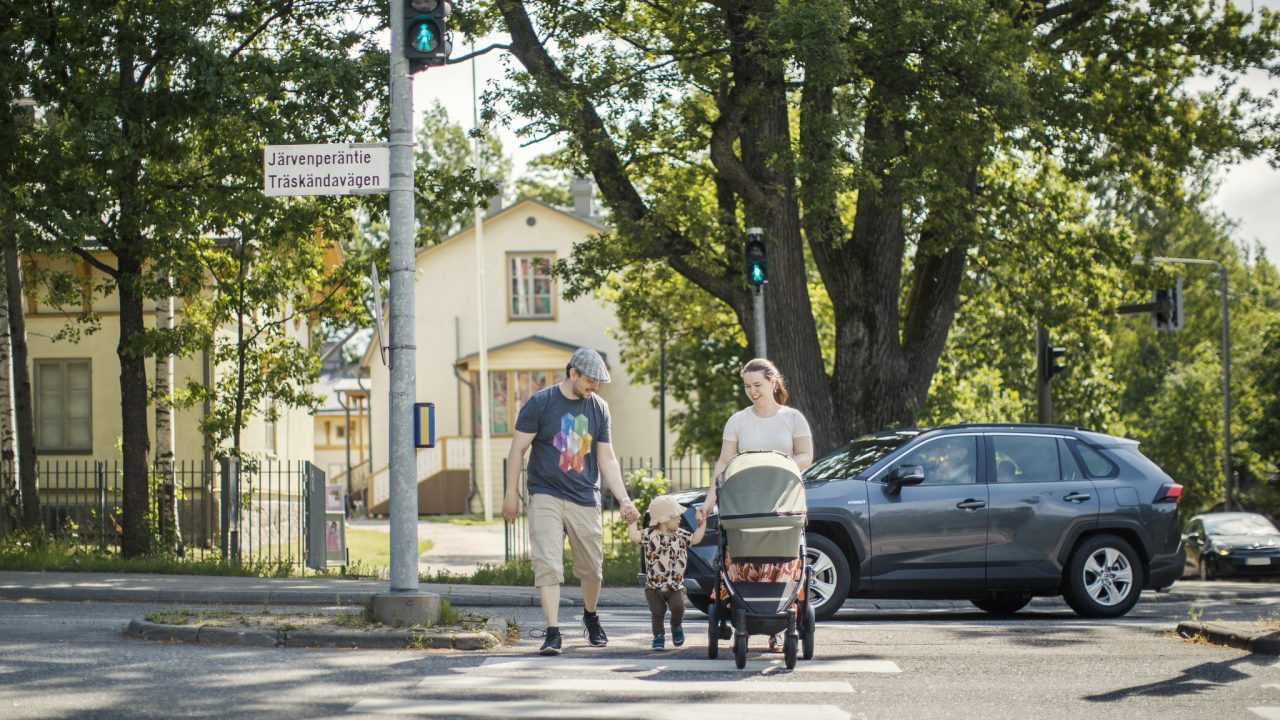 Perhe ylittää tien suojatietä pitkin.