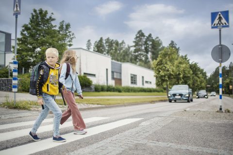 Lapset kävelevät tien yli suojatietä pitkin. Autojono lähestyy.