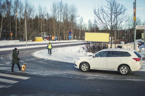 Autoilija pysähtyneenä suojatien eteen. Jalankulkija ja pyöräilijä ylittävät tietä.