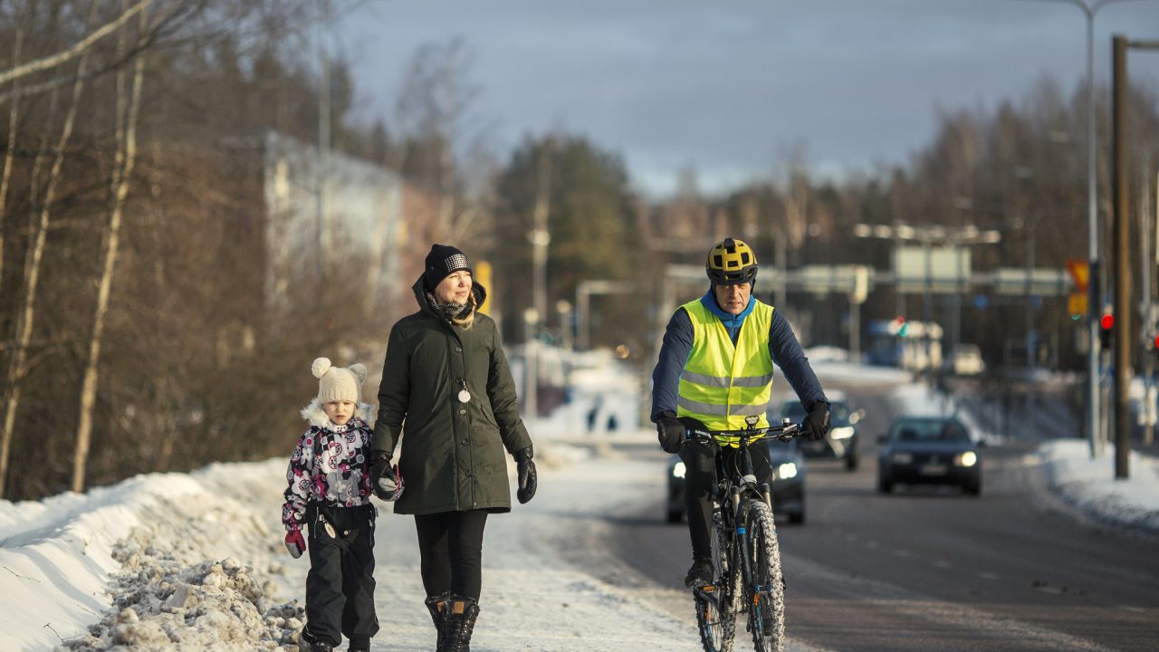 Kävelijöitä, pyöräilijä ja autoilijoita liikenteessä.