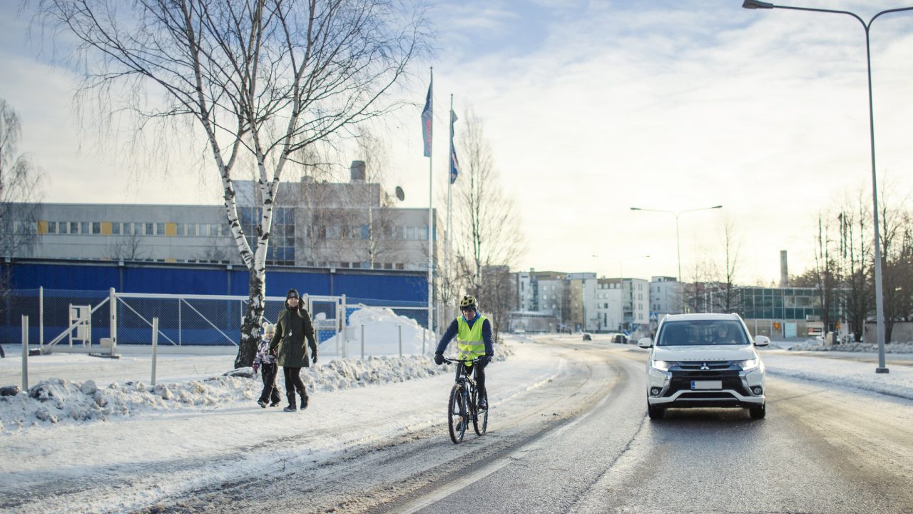 Autoilija, kävelijät ja pyöräilijät kukin kulkevat omilla kaistoillaan talvisessa maisemassa.