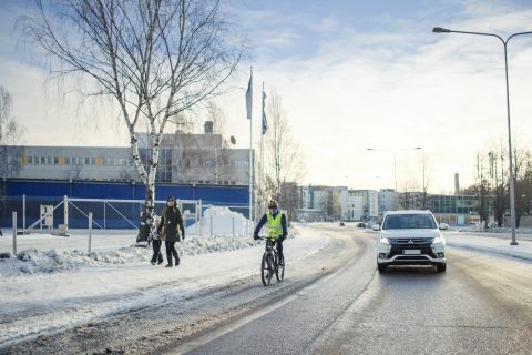 Autoilija, kävelijät ja pyöräilijät kukin kulkevat omilla kaistoillaan talvisessa maisemassa.