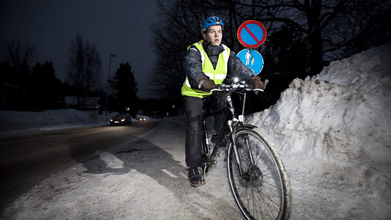 Pyöräilijä ajaa talvella pimeässä valot päällä ja turvavarusteet päällään.