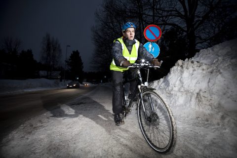 Pyöräilijä ajaa talvella pimeässä valot päällä ja turvavarusteet päällään.