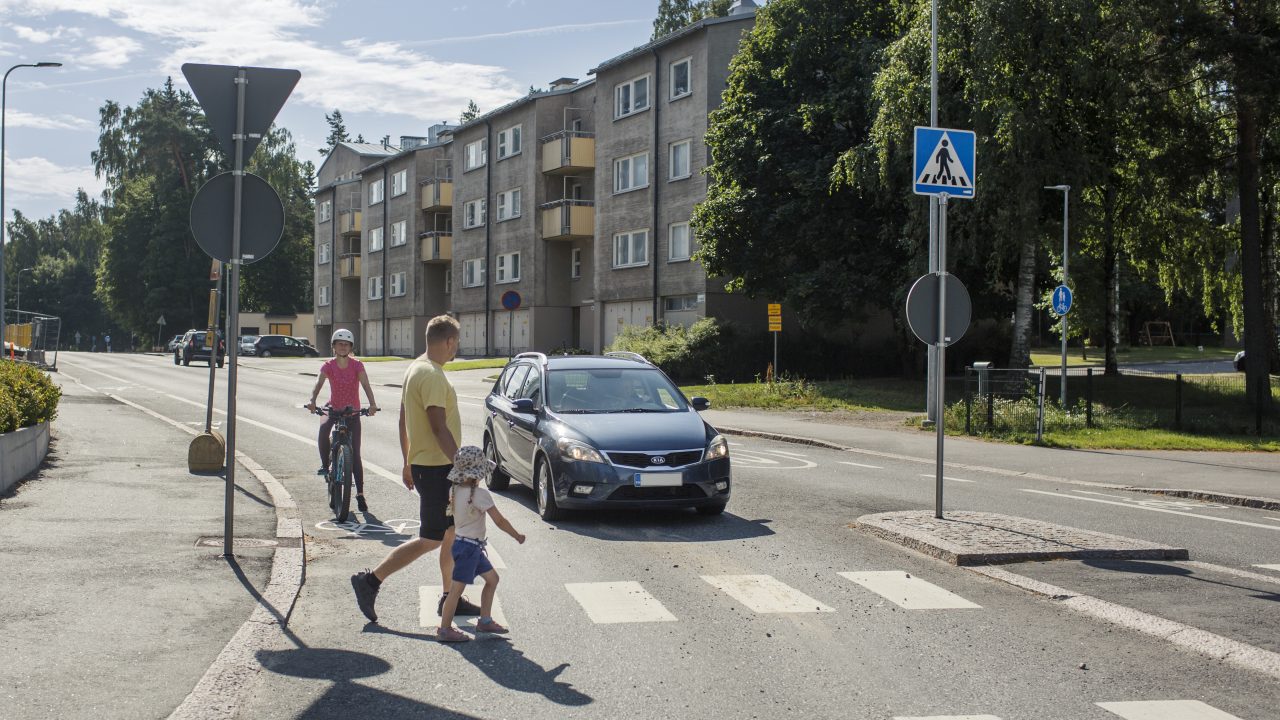 Autoilija ja pyöräilijä antavat tietä suojatietä ylittäville jalankulkijoille.