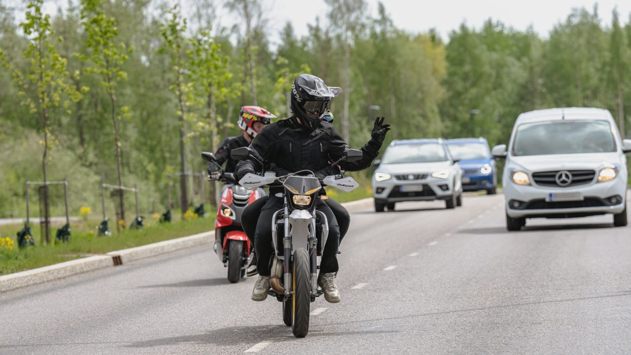 Mopoilija kiittää autoilijaa, joka antaa hänelle tietä.