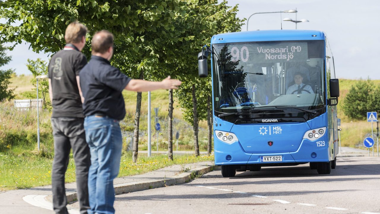 Matkustajat viittovat linja-autoa pysähtymään.