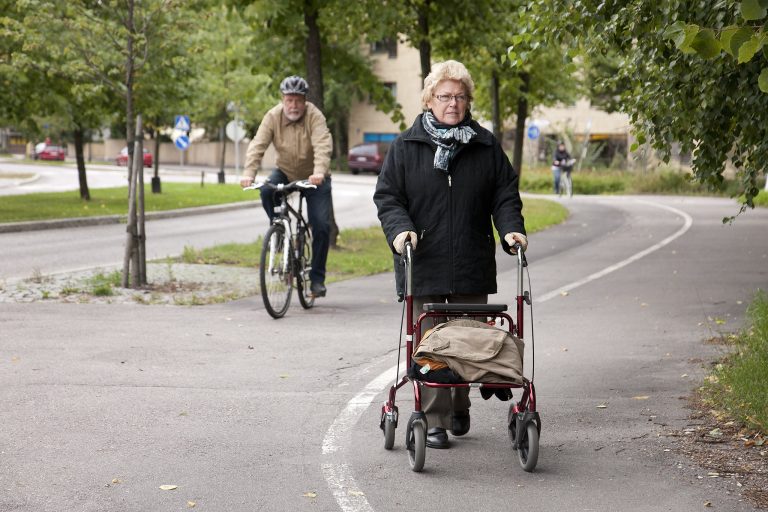Rollaattorilla liikkuva ikääntynyt ja polkupyöräilijä.