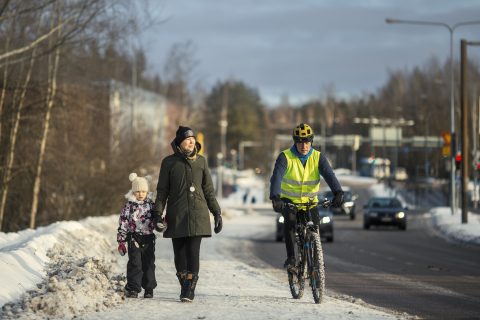 Jalankulkijat, pyöräilijä ja autoilija liikenteessä.