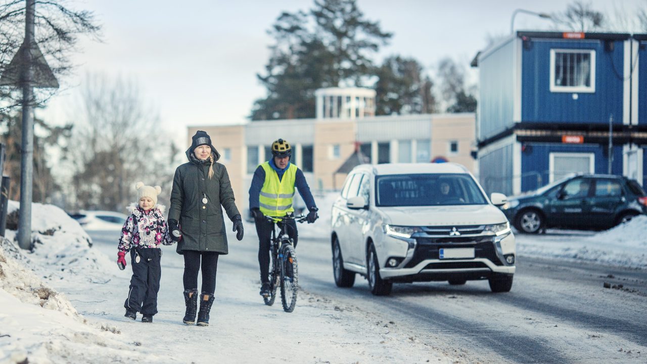 Jalankulkijat, pyöräilijä ja autoilija tien päällä.