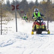 Kaksi moottorikelkkailijaa ajaa peräkkäin moottorikelkkareitillä.
