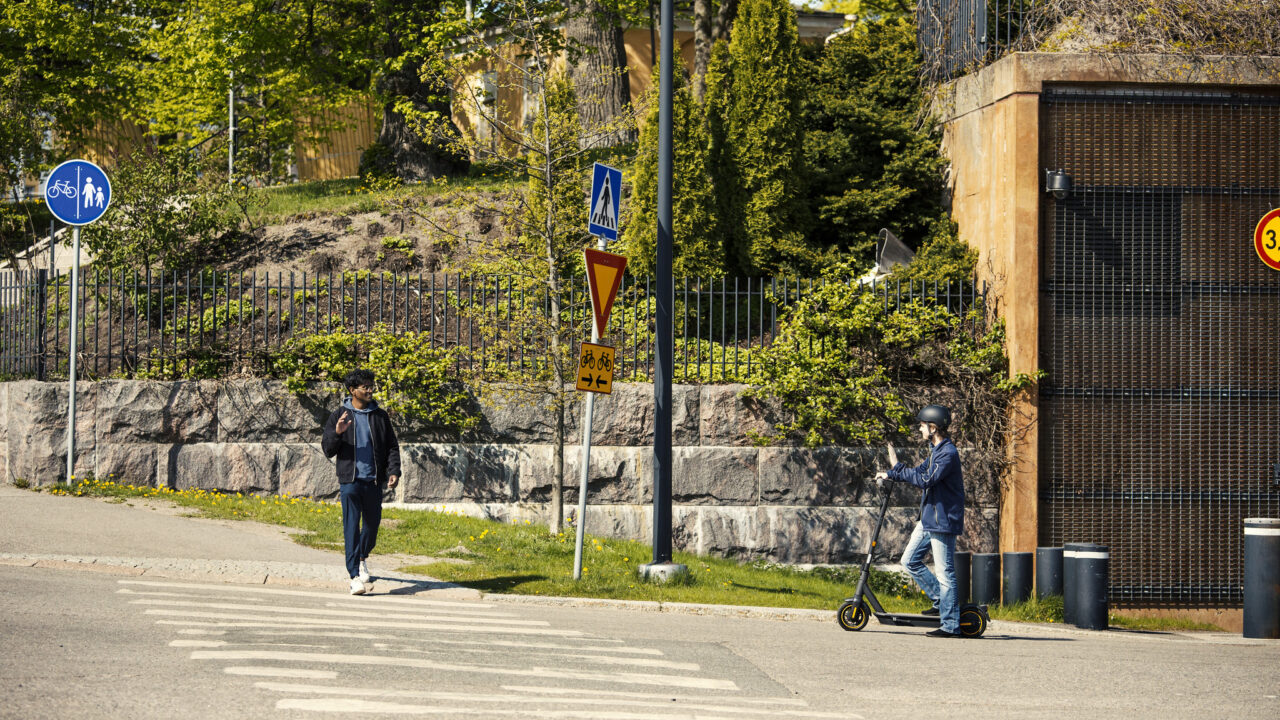 Sähköpotkulautailija antaa tietä suojatietä ylittävälle jalankulkijalle.