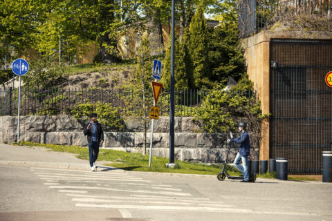 Sähköpotkulautailija antaa tietä suojatietä ylittävälle jalankulkijalle.